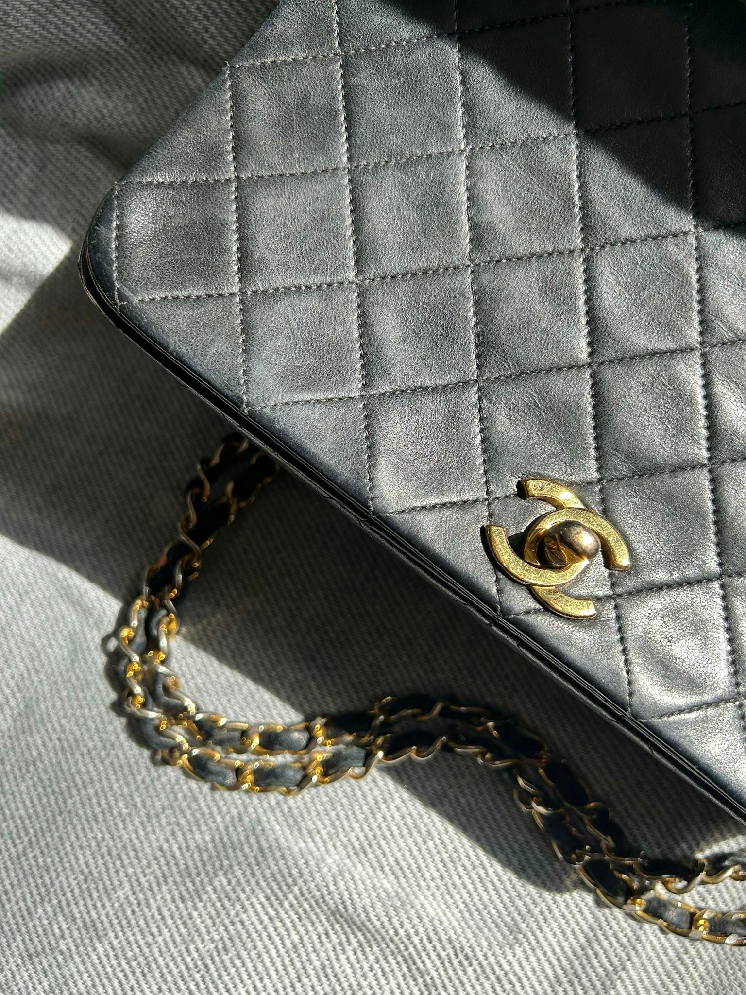Close-up of a luxury quilted black leather handbag with gold chain strap and logo.